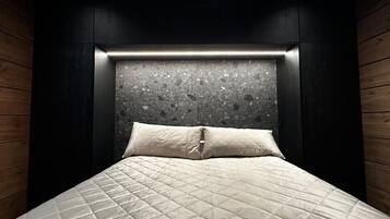 Een bed met een gebogen, beige deken en een hoofdbord met een structuur die doet denken aan steen.