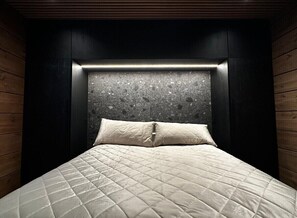 A bed with a quilted beige cover and a headboard with a textured stone-like design.