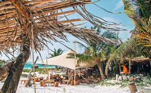 A beachside restaurant with outdoor seating, palm trees, and a thatched-roof structure. - Sleeps 6 w Private Rooftop Pool & 2 Bikes (Tulum)