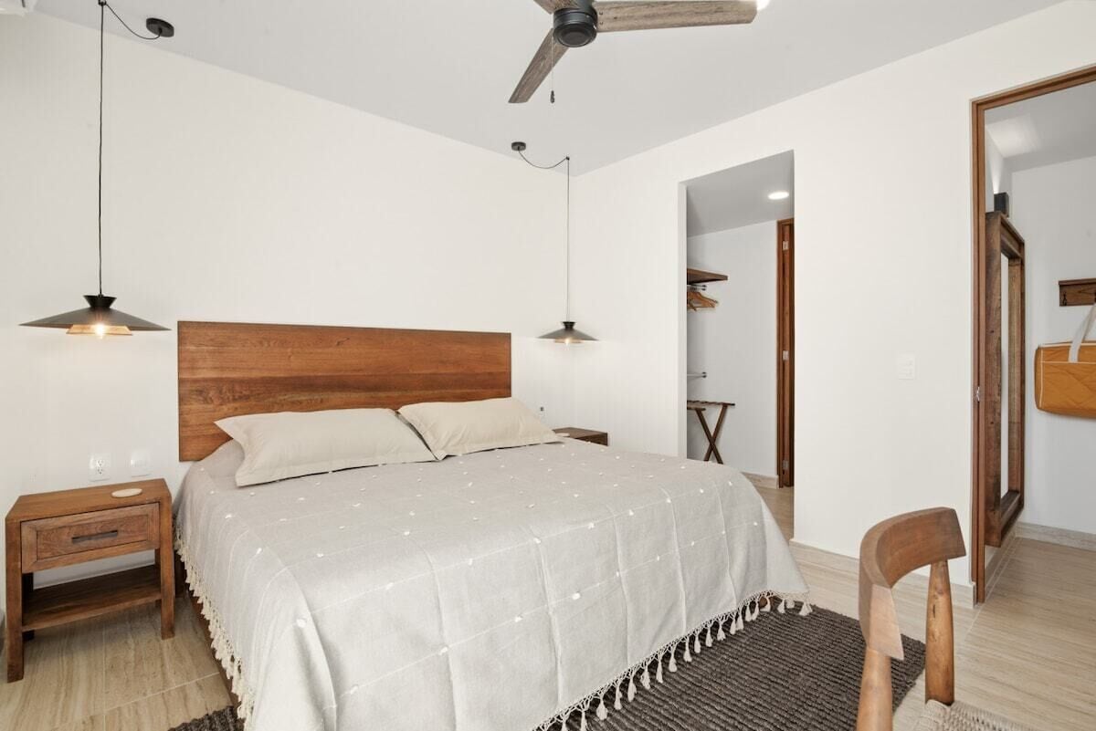 Ein Schlafzimmer mit einem hölzernen Kopfteil, einem Bett mit weißer Bettdecke, zwei Nachttischen, einer Stehlampe und einem Deckenventilator.