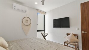 A bedroom with a bed, a television mounted on the wall, a chair, and an air conditioning unit. - Ts'íibol: 3BR w Private Rooftop Deck & Pool (Tulum)