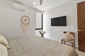 A bedroom with a bed, a television mounted on the wall, a chair, and an air conditioning unit. - Ts'íibol: 3BR w Private Rooftop Deck & Pool (Tulum)