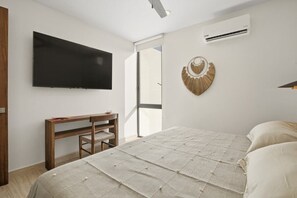 A bedroom with a bed, a TV mounted on the wall, a wooden bedside table, and an air conditioning unit. - Ts'íibol: 3BR w Private Rooftop Deck & Pool (Tulum)