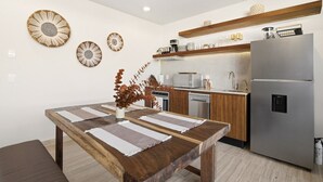 A modern kitchen with a wooden table, stainless steel appliances, and decorative wall art. - Ts'íibol: 3BR w Private Rooftop Deck & Pool (Tulum)
