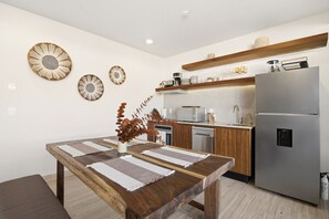A modern kitchen with a wooden table, stainless steel appliances, and decorative wall art. - Ts'íibol: 3BR w Private Rooftop Deck & Pool (Tulum)