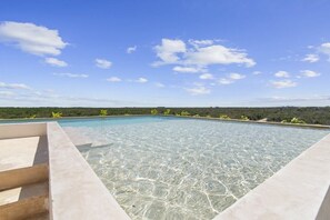 A clear swimming pool with steps leading into it, surrounded by a clear sky and distant greenery. - Ts'íibol: 3BR w Private Rooftop Deck & Pool (Tulum)