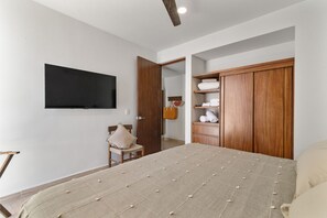 A bedroom with a bed, a chair, a wardrobe, and a television on the wall. - Sleeps 6 w Private Rooftop Pool & 2 Bikes (Tulum)