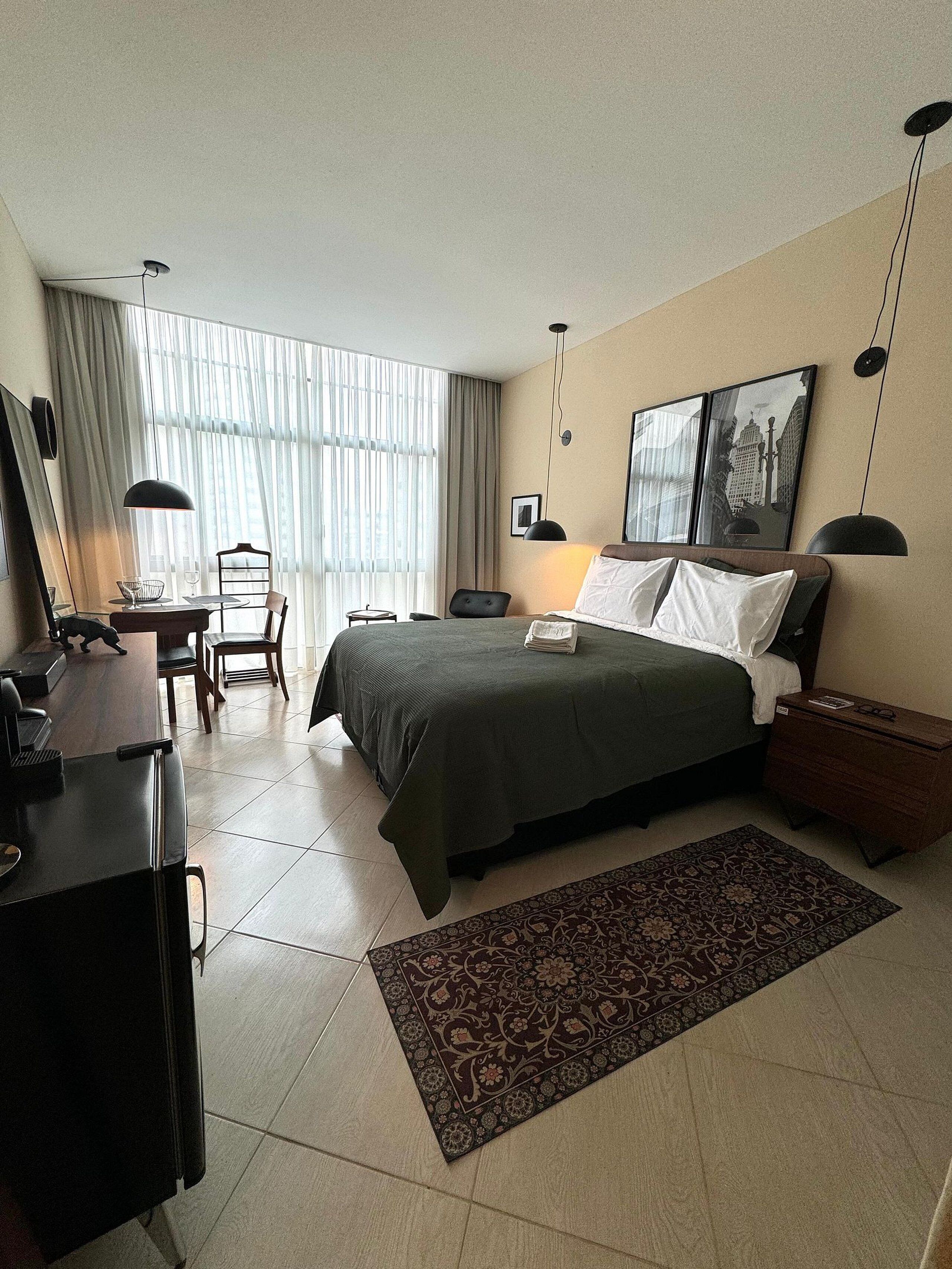 A hotel room with a bed, a desk, a chair, a small table, and a rug.