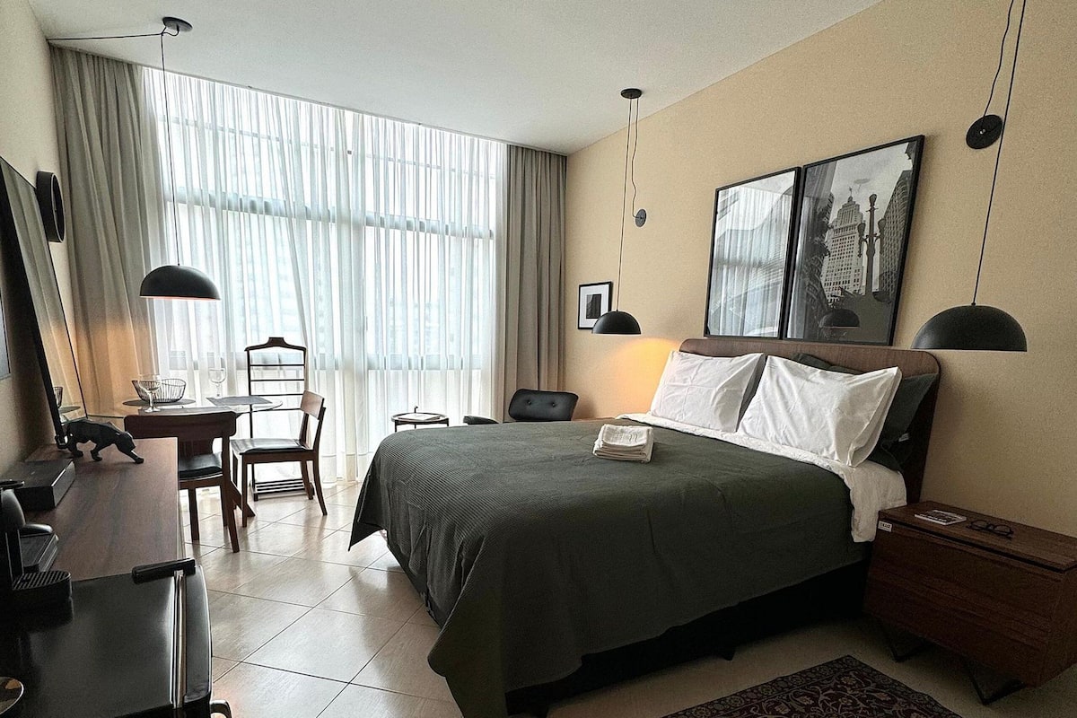 A hotel room with a bed, a desk, a chair, a small table, and a rug.