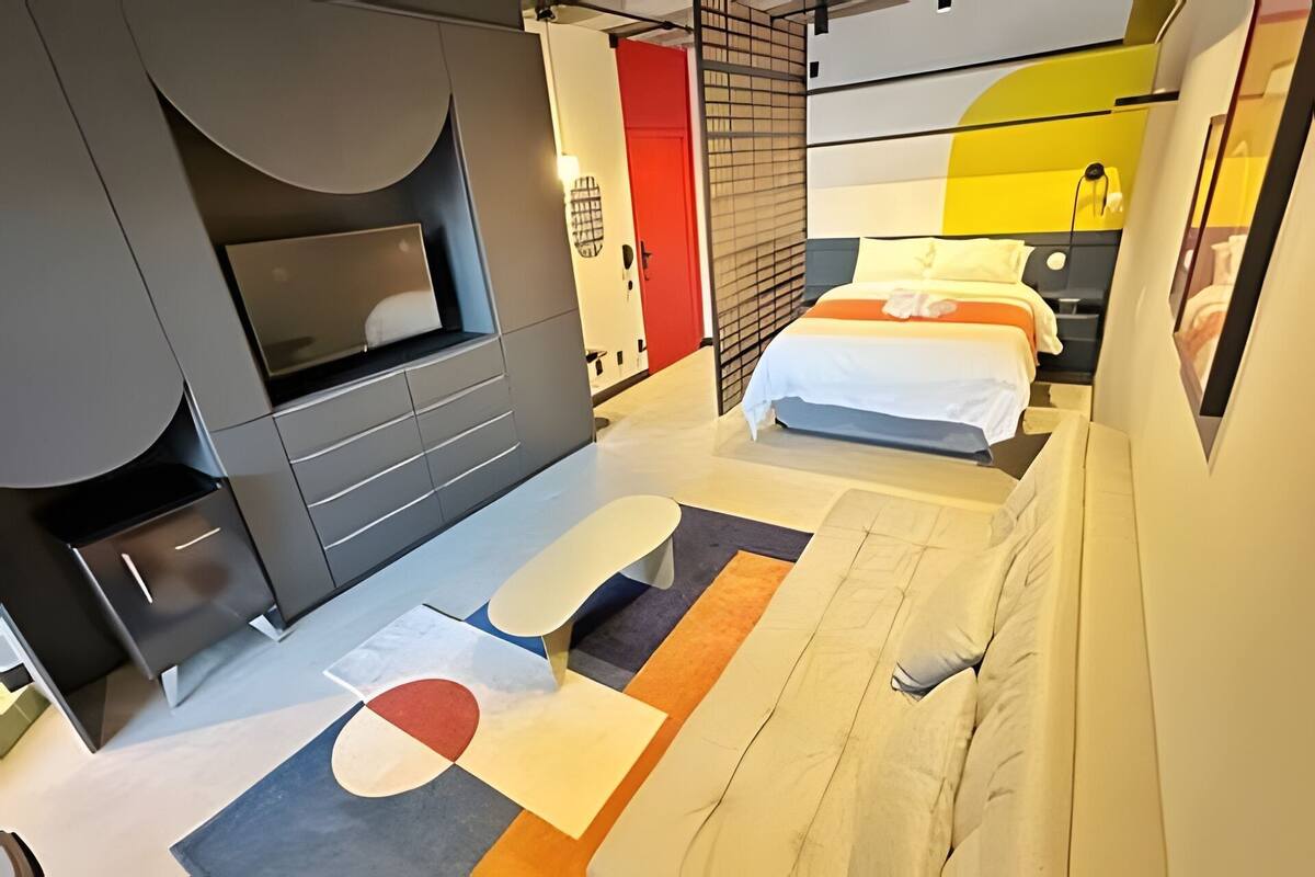 A modern hotel room with a bed, a TV, a desk, and a bathroom.