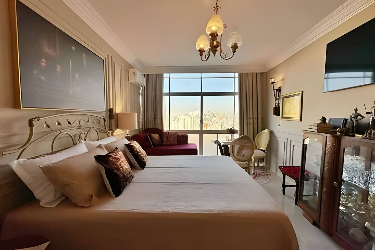 A hotel room with a large bed, a desk, a chair, and a view of the city.
