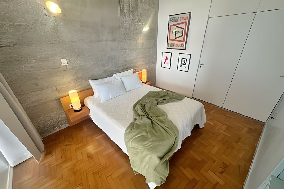 A bedroom with a bed, bedside lamps, a wardrobe, and a wall with framed pictures.