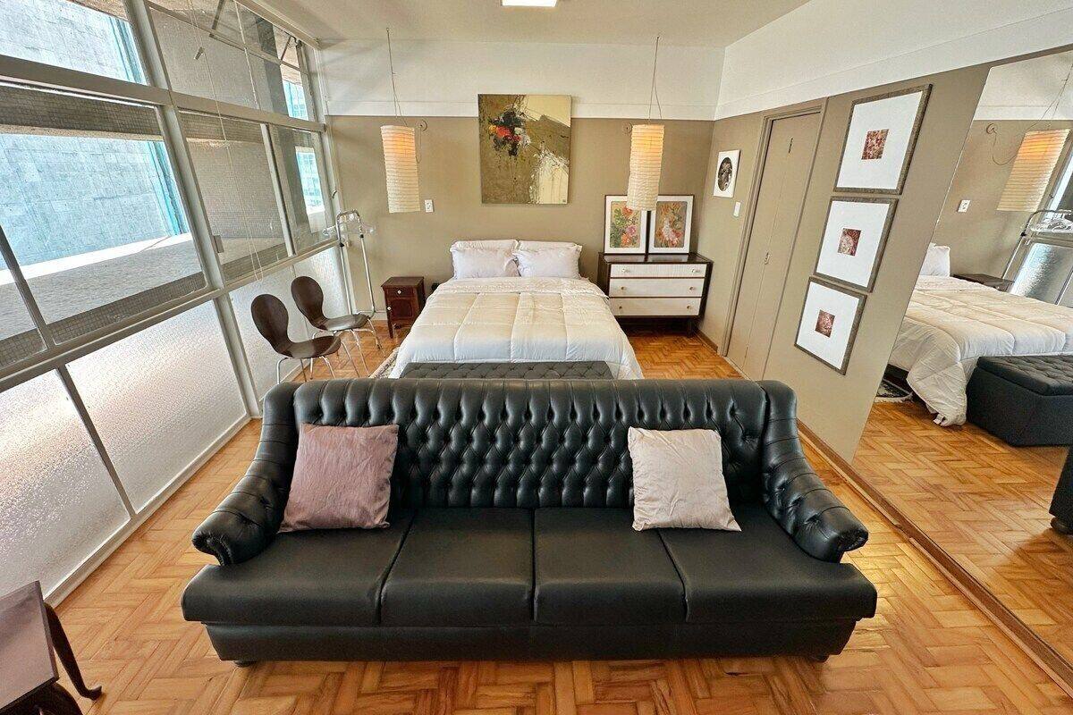A modern hotel room with a large window, a black leather sofa, a bed, and a small desk.