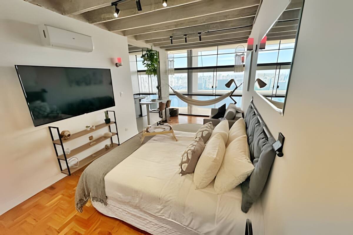 A modern bedroom with a large bed, a TV, and a hammock.
