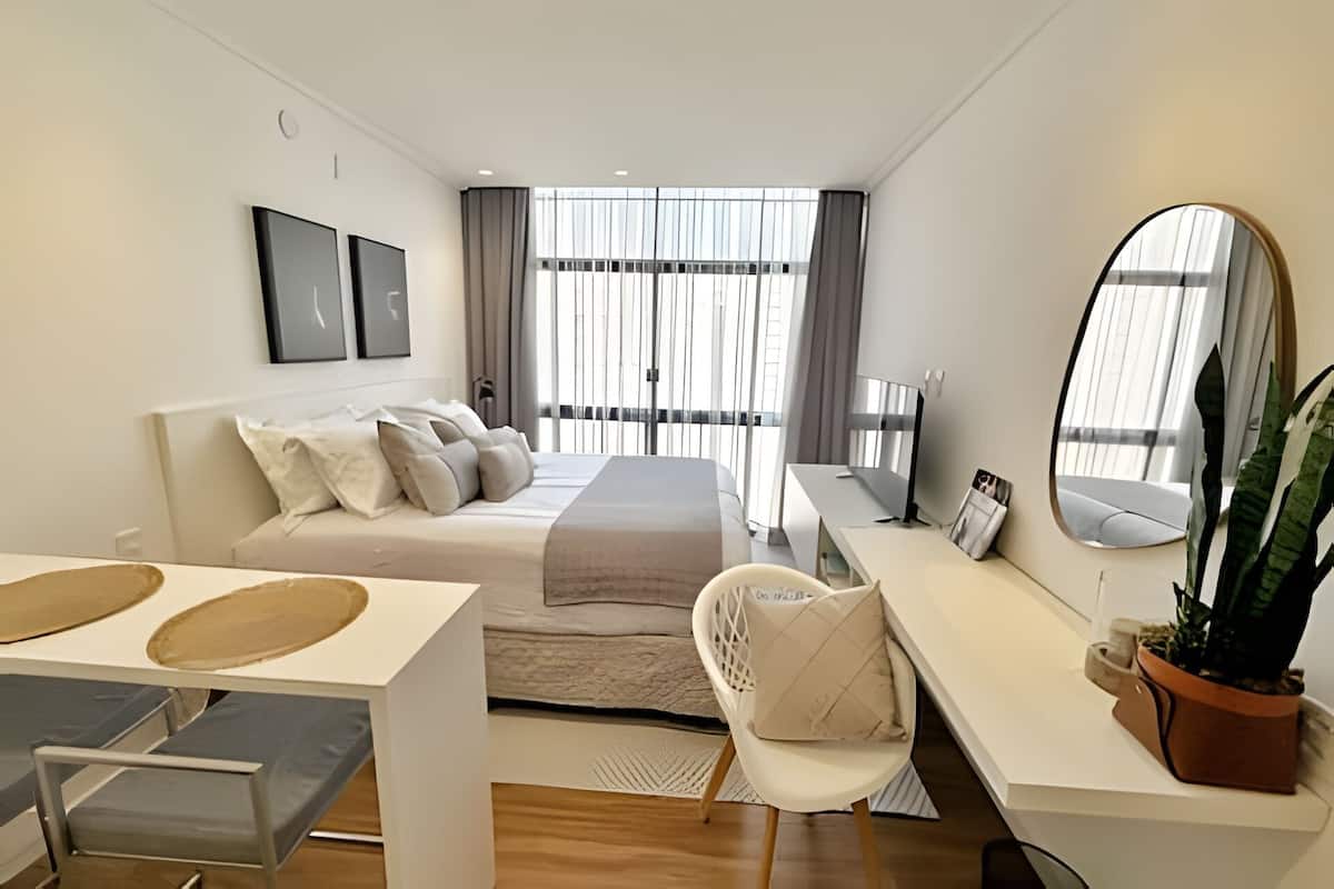 A modern bedroom with a bed, bedside table, chair, desk, and a large mirror.