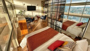 A modern bedroom with two beds, a desk, and a large window offering a city view. - Vem pro Copan (São Paulo)
