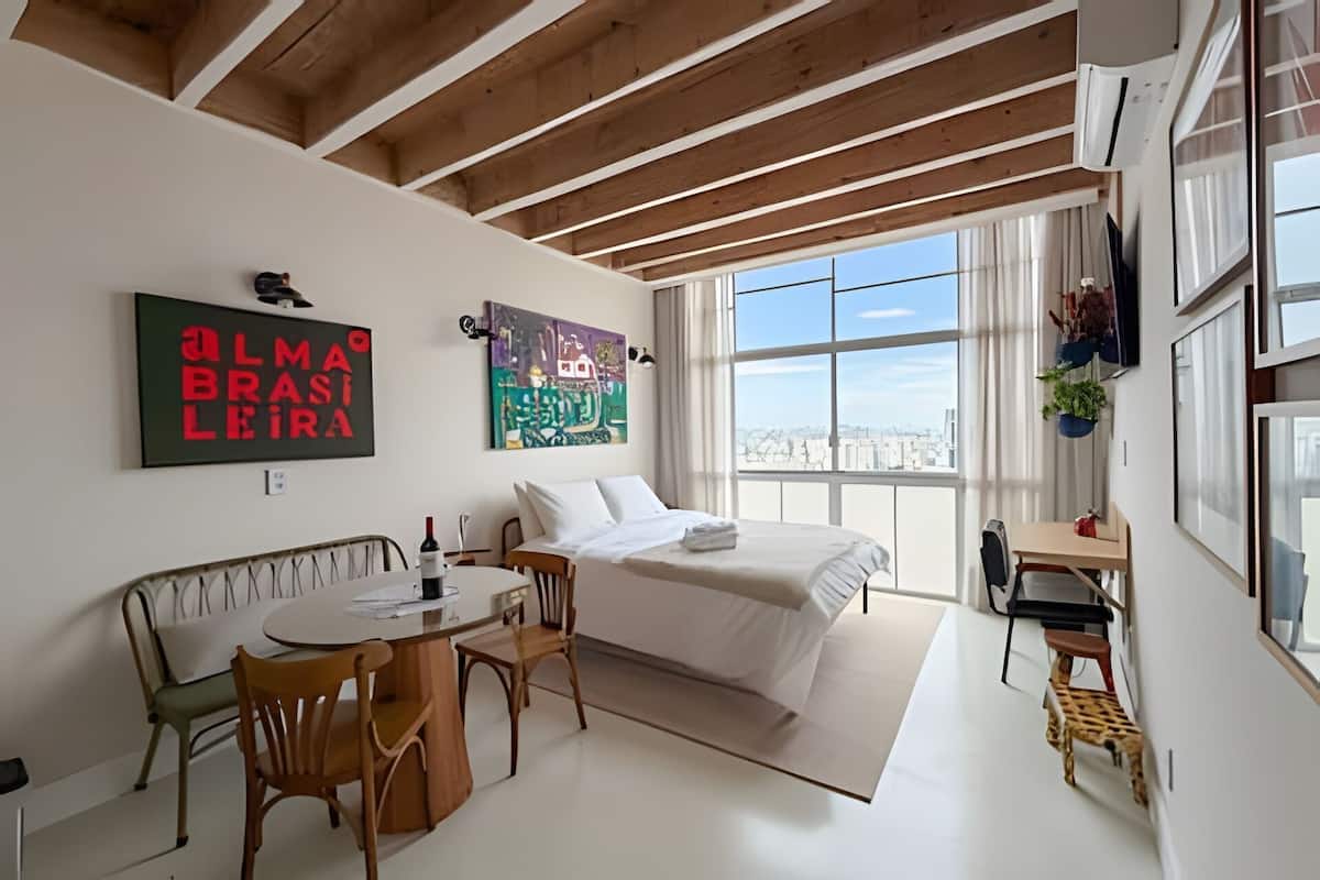 A modern bedroom with a large window, a bed, a desk, and a dining area.