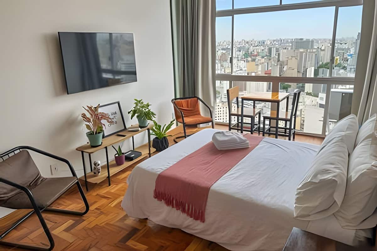 A hotel room with a bed, a desk, a chair, and a view of the city.