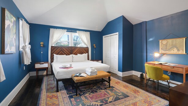 A bedroom with a bed, bedside table, lamp, chair, desk, and a large rug. - Cute and Cozy 2BR/2BA w/Parking, Yard, King Suite & Blocks to Local Favorites (New Orleans)