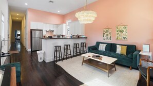 A modern kitchen with white cabinets, a stainless steel refrigerator, and a bar area with stools. - Cute and Cozy 2BR/2BA w/Parking, Yard, King Suite & Blocks to Local Favorites (New Orleans)