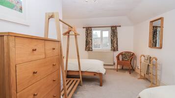 Un dormitorio con un aparador de madera, una cama con estructura de madera, una silla, un tendedero de madera y una ventana con cortinas.