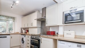 Una cocina moderna con armarios blancos, horno empotrado, microondas y lavadora.