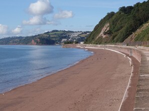 A sandy beach with a curved stone wall, a clear sky, and hills in the background. - Orchard Cottage (Dawlish)