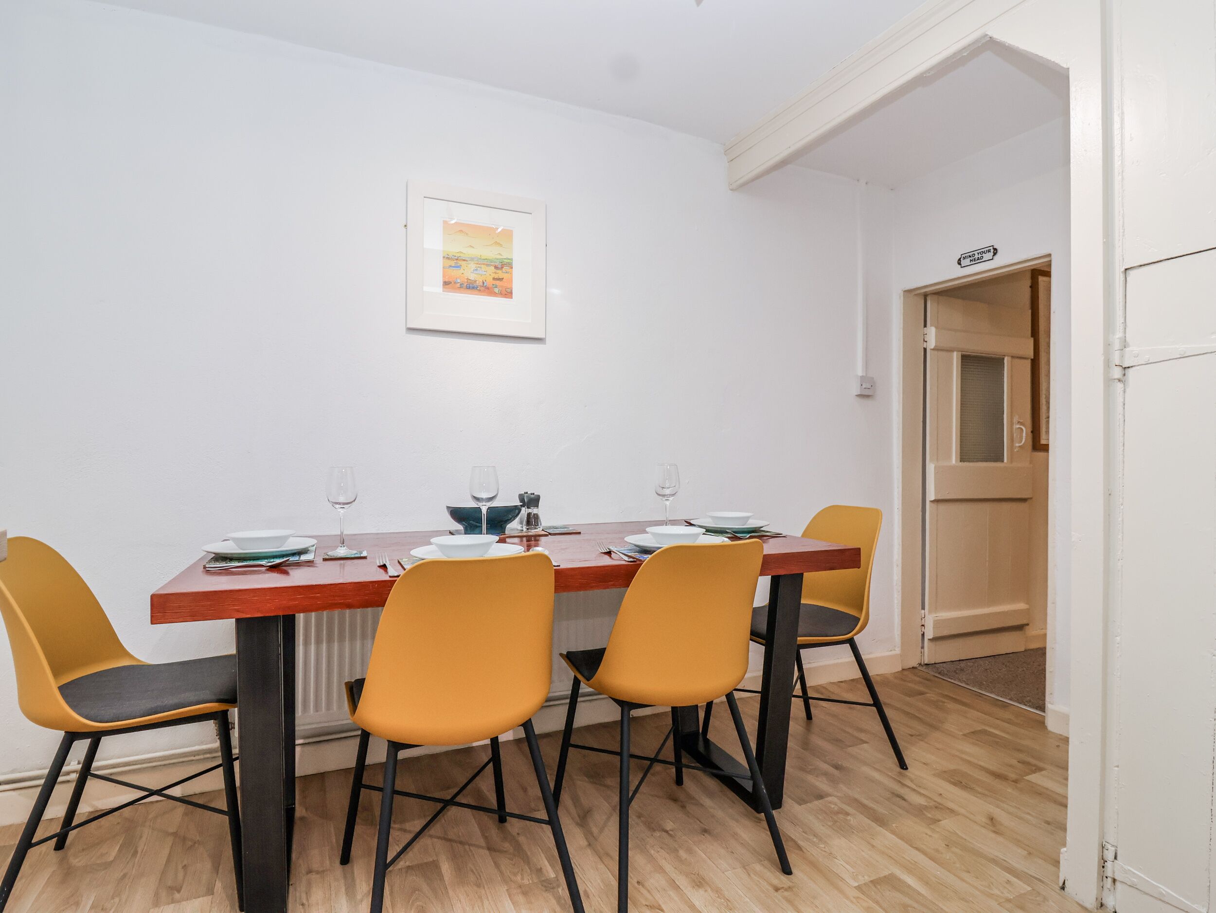 Uma sala de jantar com uma mesa de madeira, quatro cadeiras amarelas e um quadro na parede.