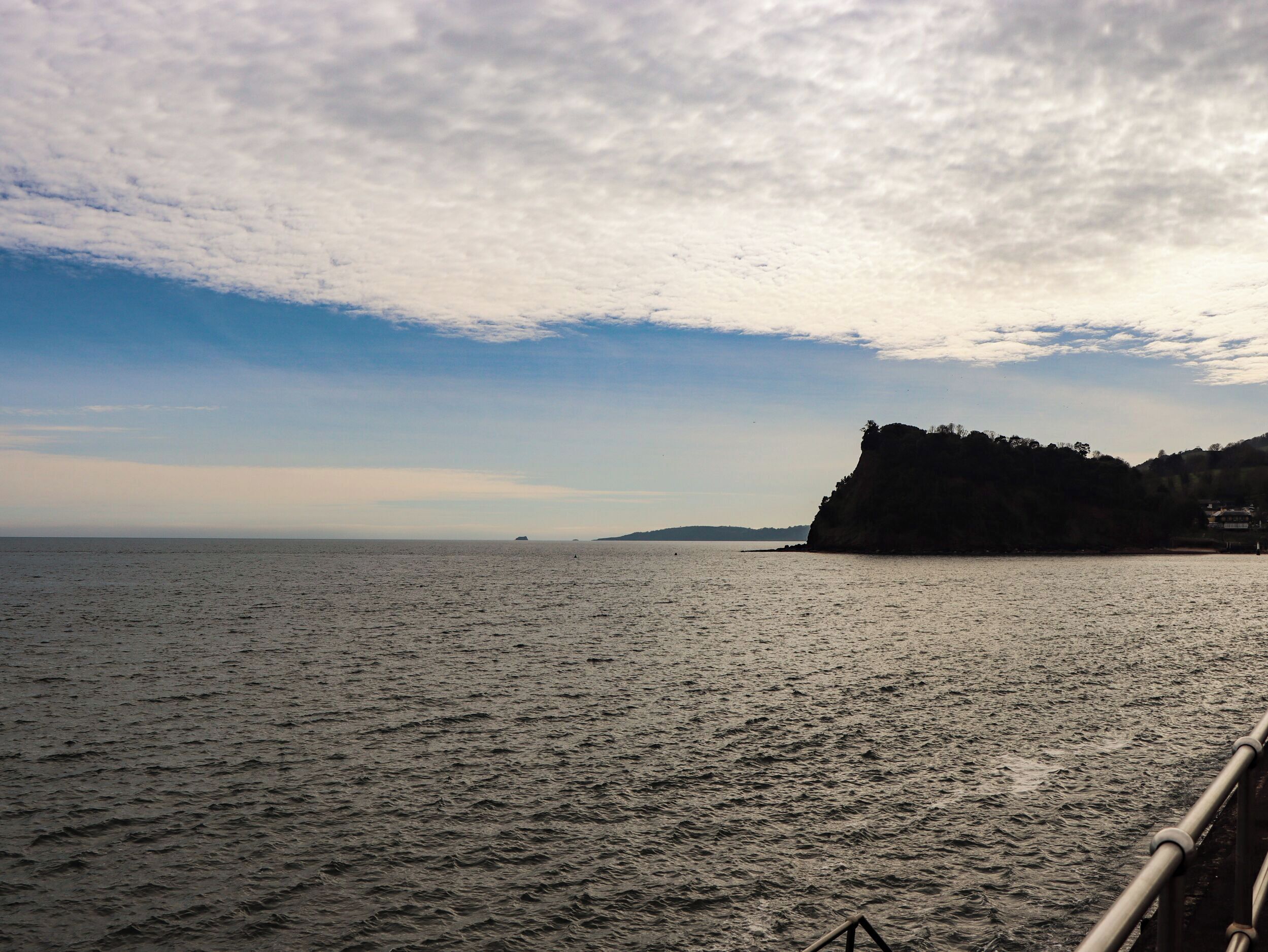 A coastal view with a rocky cliff and calm sea.