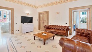 Ein großzügiges Wohnzimmer mit einer Ledersofa, einem Couchtisch und einem an der Wand befestigten Flachbildfernseher.