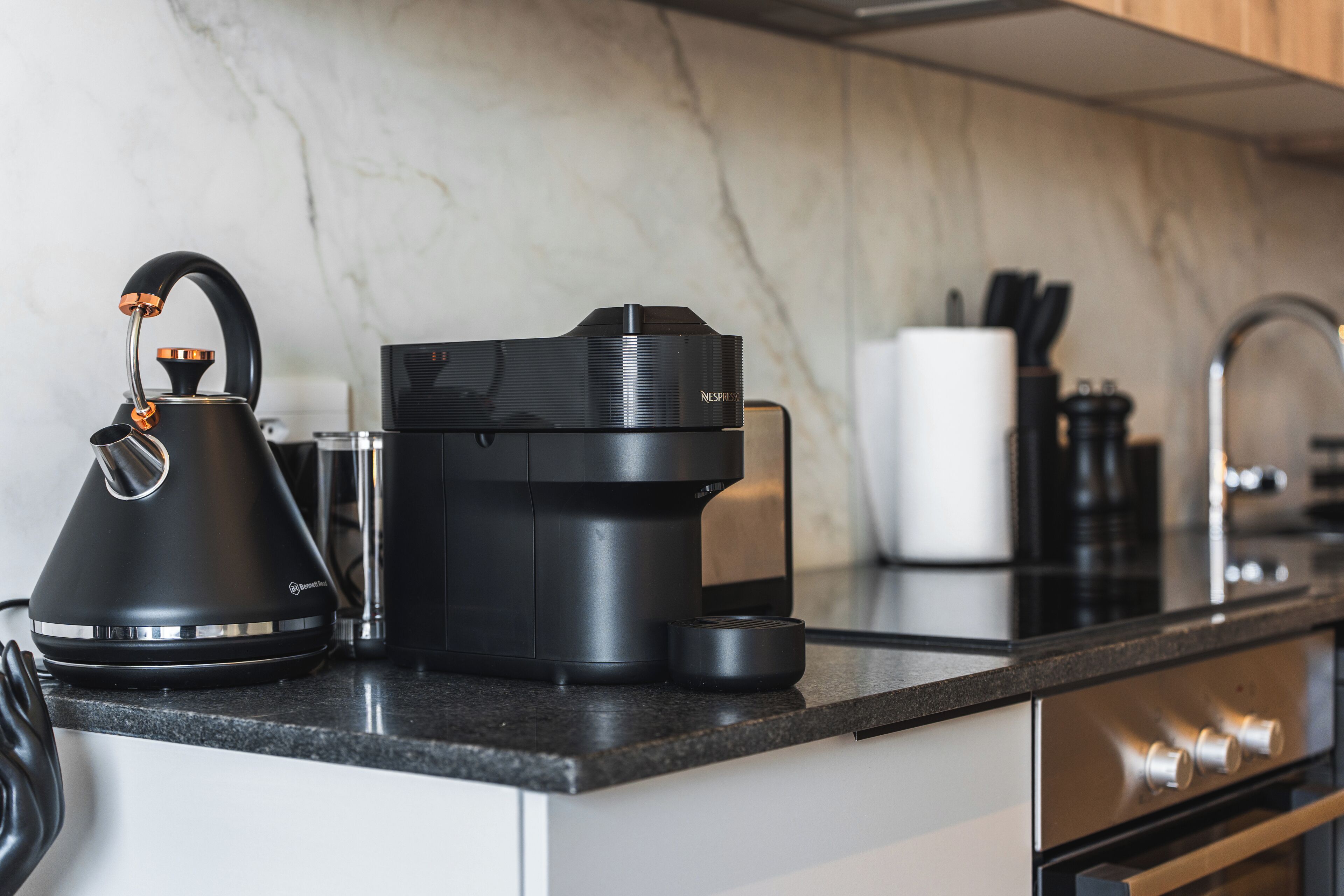 A modern kitchen with a coffee maker, kettle, and a coffee pod holder on the counter.
