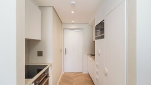 Un couloir étroit avec un parquet en bois disposé en chevrons, des murs blancs et une porte blanche au fond.