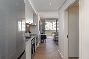 A narrow hallway with a kitchen on one side, a dining area with a table and chairs, and a view of buildings outside. - Dolce Vita | Stylish Sea Point Apartment (Cape Town)