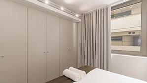 A hotel room with a bed, a wardrobe, and a window with curtains. - Dolce Vita | Stylish Sea Point Apartment (Cape Town)