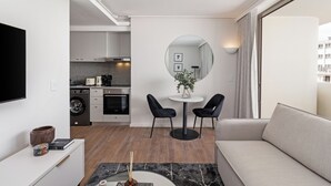 A modern living room with a sofa, a round table with two chairs, a TV mounted on the wall, and a kitchen in the background. - Dolce Vita | Stylish Sea Point Apartment (Cape Town)