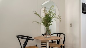 Zona pranzo con tavolo rotondo, due sedie nere con seduta intrecciata e un vaso con piante verdi.