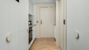 Un corridoio stretto con pavimento in parquet a spina di pesce, pareti bianche e una porta chiusa in fondo.
