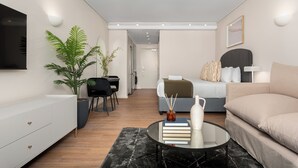 Un soggiorno moderno e luminoso con divano, tavolino, televisione, zona pranzo con tavolo e sedie, e camera da letto con letto e comodino.
