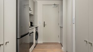Un couloir étroit avec un réfrigérateur en acier inoxydable, un lave-linge et une porte au fond.