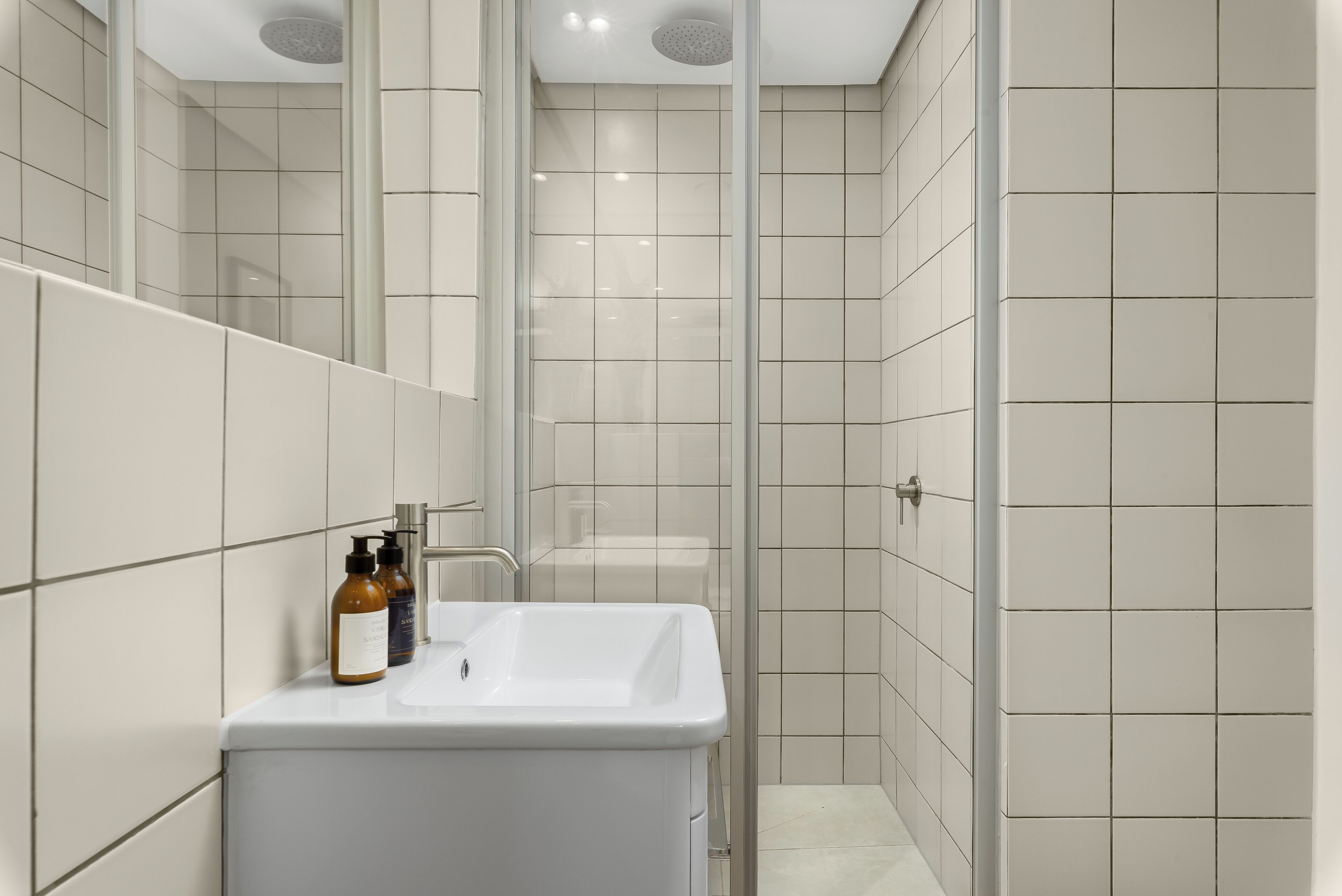 Un bany modern amb un lavabo blanc, un mirall i parets revestides de rajoles.
