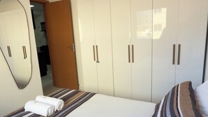 A bedroom with a large bed, a wardrobe with multiple doors, a mirror, and a door leading to another room. - Refúgio Luxo •novo, piscina, central, ar condicionado (Montes Claros)