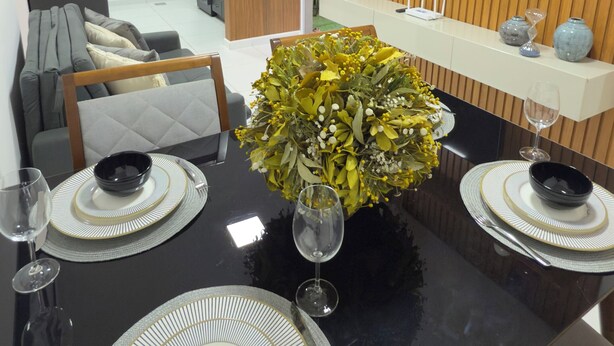 A modern dining area with a black table set for four, surrounded by wooden paneling and a mounted TV. - Refúgio Luxo •novo, piscina, central, ar condicionado (Montes Claros)