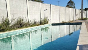 A long, narrow swimming pool with clear blue water, surrounded by a concrete wall and a tiled deck. - Refúgio Luxo •novo, piscina, central, ar condicionado (Montes Claros)