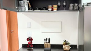 A compact kitchen with a black countertop, a coffee maker, and various kitchen utensils. - Refúgio Luxo •novo, piscina, central, ar condicionado (Montes Claros)