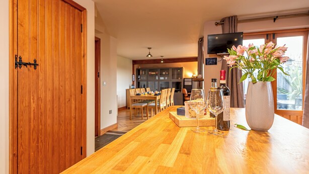 Een houten eettafel met een bloemenvaas, wijnglazen en flessen.