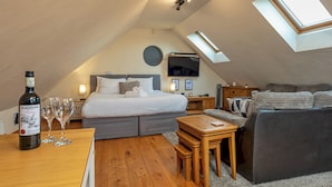 Een gezellig, goed verlichte zolderkamer met een bed, een bank, een klein tafeltje en een televisie.
