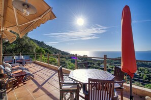 Une terrasse avec une table et des chaises, un parasol rouge et une vue sur la mer.
