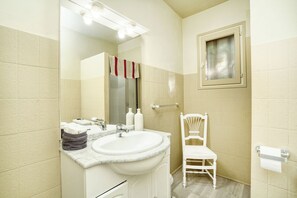Ein Badezimmer mit Waschbecken, Spiegel und Stuhl, alles in Weiß.