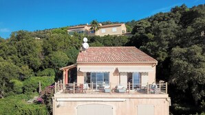 Ein Gebäude mit rotem Ziegeldach, einem Balkon mit Sitzgelegenheiten und Blick auf einen Hügel mit weiteren Gebäuden.