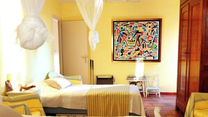 Ein Hotelzimmer mit zwei Betten, einem Nachttisch, einem Sessel, einem Schreibtisch und einem großen, farbenfrohen Bild an der Wand.